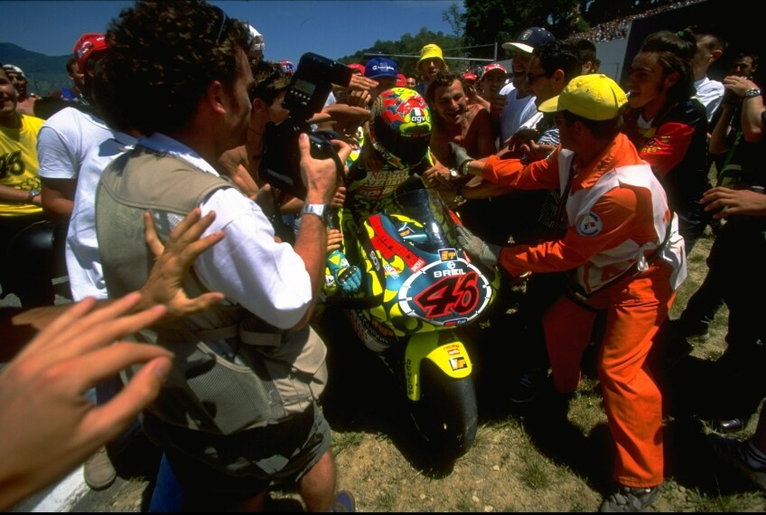 L’arrivo in impennata, il bagno di tifosi che invadono il circuito e la caduta nel giro d’onore per Valentino Rossi dopo lo scontro con il fotografo Gigi Soldano.