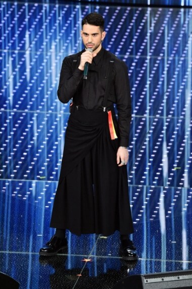 Ecco il look originale del cantante che indossa un completo total black con pettorina, camicia nera e un pantalone extra large simile ad una gonna. Completa il look un particolare anello legato ad un bracciale da una catena.