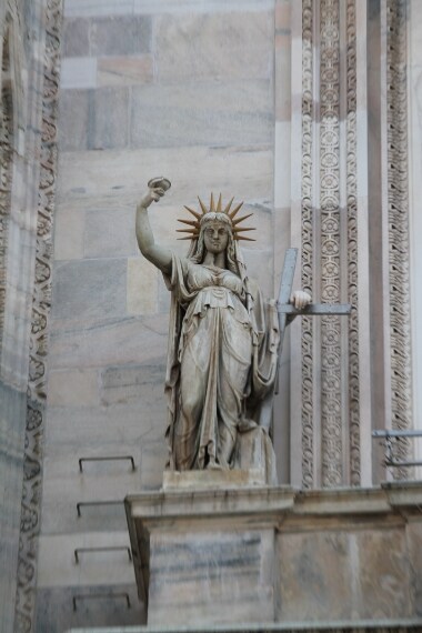 Tra le statue del Duomo, sul balcone sopra l’ingresso centrale della cattedrale, si trova La Legge Nuova, eseguita nel 1810 da C. Pacetti. Secondo la leggenda, la figura femminile con il braccio alzato, la torcia in mano e quella corona di punte intorno al capo sarebbe stata presa a modello per la Statua della Libertà realizzata da Bartholdi nel 1885 per New York.