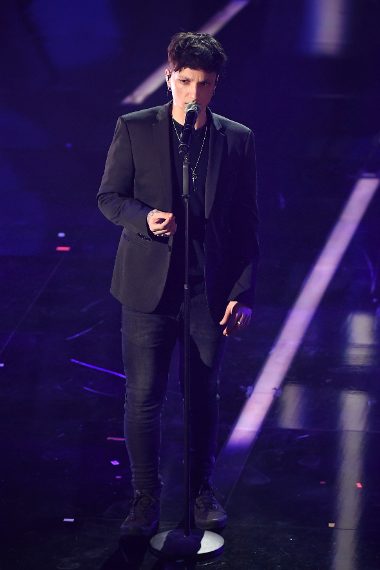 Questa sera il giovane cantante sceglie un completo classico scuro indossato su pull scuro