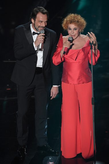 Lui elegante in nero, lei con completo rosso dal top geometrico