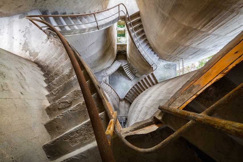 Il vecchio Cementificio SACCI fu creato nel dicembre 1933 dalla fusione di diverse piccole ditte locali che producevano leganti idraulici e calcestruzzo preconfezionato. La fabbrica ha svolto un ruolo fondamentale nell’economia e nello sviluppo abitativo dell’area circostante. Durante la Seconda guerra mondiale subì danni importanti. I lavori di ricostruzione iniziarono con un programma di restauro completo per ripristinare il potenziale di produzione e distribuzione di cemento grigio e bianco,