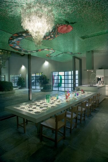 Propaggine del cortile è l’ambiente cucina, su cui domina oltre che un lampadario di Deborah Thomas realizzato con cocci di cristalli infranti, anche una spettacolare rappresentazione in mosaico del Serpante Biblico opera del maestro Sandro Chia (prod. Bisazza). Le pareti sono decorate con stucchi in gesso a decori floreali (prod. Sadi). Il grande tavolo disegnato da Fabio Novembre, così come il corpo cucina (prod. Boffi Italia), sono interamente rivestiti in Corian (prod. DuPont), che pantogr
