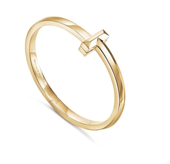 Bracciale in oro giallo a cerchio, con incisione interna e chiusura superiore che richiama l'iconico motivo a "T".
