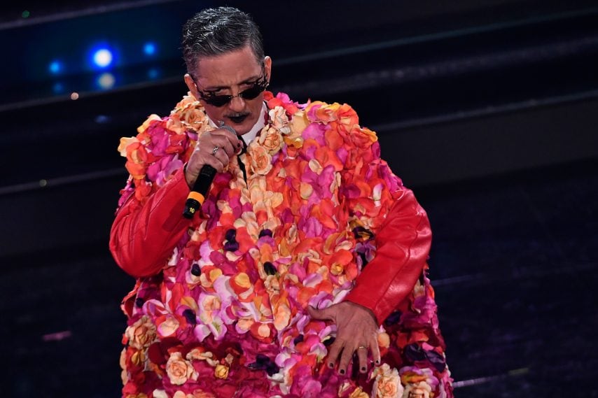 Il conduttore sale sul palco con un mantello floreale, occhiali da sole dalla forma originale e con le labbra dipinte di nero