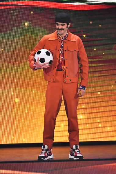 Il cantante indossa un originale completo arancione con una camicia a fantasia