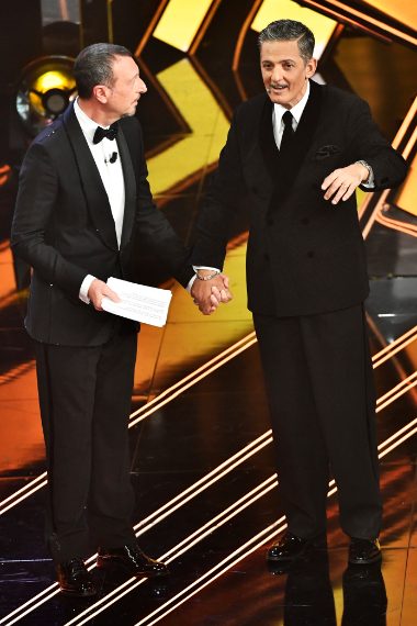 Il conduttore è elegantissimo con un completo doppiopetto dai baveri a scialle in velluto nero