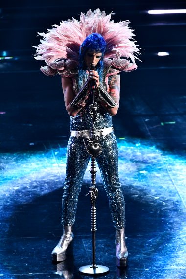 Il performer indossa una tuta di paillettes argentate con piume rosa a "armatura" da rugby