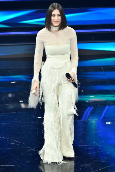 Total white per la cantante che indossa un corsetto e pantaloni a zampa di seta con lunghe frange