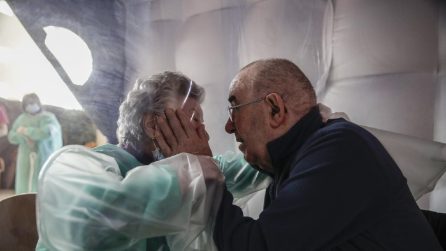 L'abbraccio tra il marito ricoverato e la moglie: separati dalla protezione in plastica