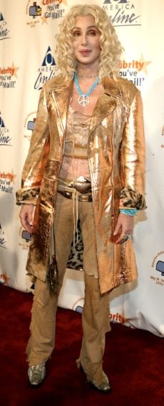 La cantante indossa un cappotto color oro con fodera maculata, pantaloni scamosciati a vita bassa e una collana con il simbolo della pace