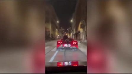 Parla al telefono seduto sul cofano di una Ferrari in movimento per le strade di Milano